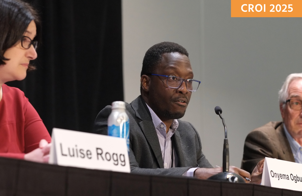 Dr Onyema Ogbuagu at a media briefing at CROI 2025. He is sitting between two people and talking into a microphone.