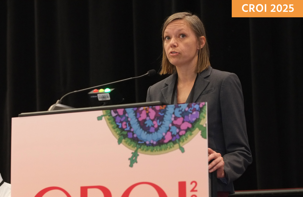 Dr Mackenzie Cottrell presenting at CROI 2025. She is standing behind a lectern and talking into a microphone.