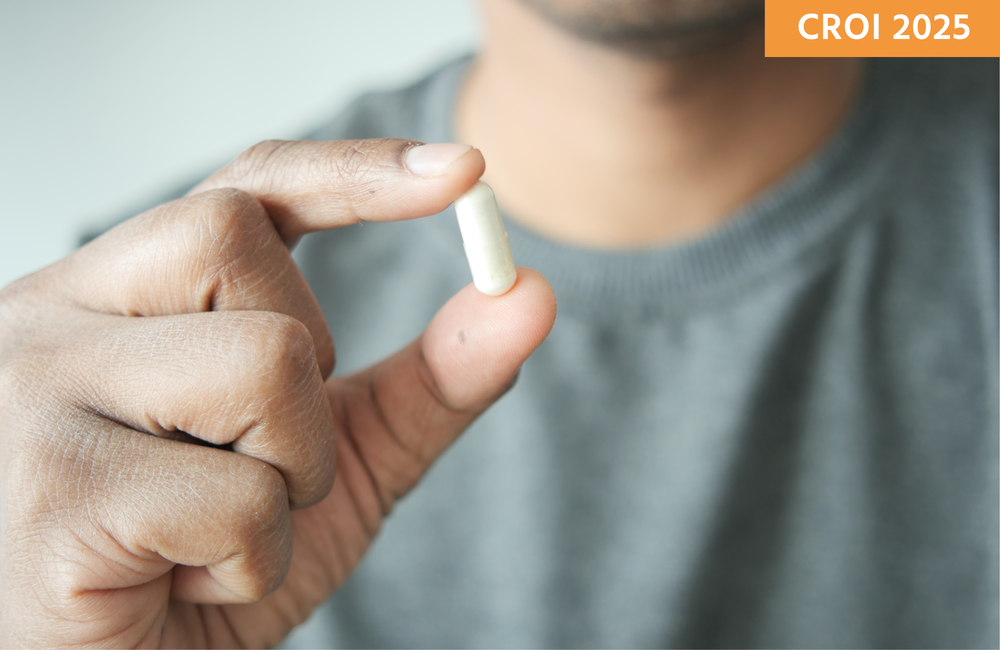 A person in a grey tshirt holding a white pill.