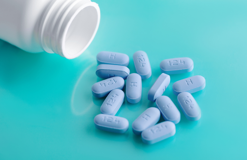 Image: iStock A white bottle of pills is on its side with blue PrEP pills spilling out, on a turquoise background